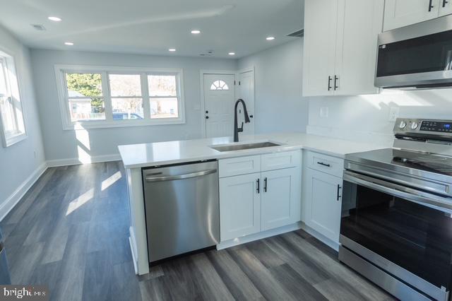 kitchen with white cabinetry, sink, dark hardwood / wood-style flooring, kitchen peninsula, and appliances with stainless steel finishes