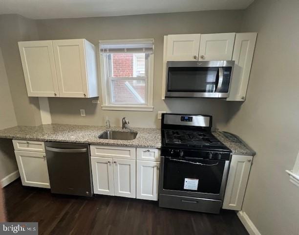 kitchen with light stone countertops, white cabinets, appliances with stainless steel finishes, sink, and dark hardwood / wood-style floors