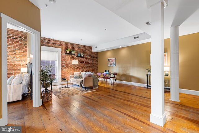 living room with decorative columns, hardwood / wood-style floors, and brick wall