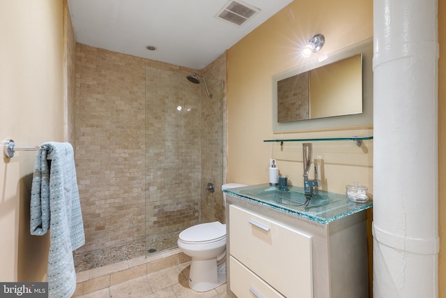 bathroom featuring tile patterned flooring, tiled shower, toilet, and vanity