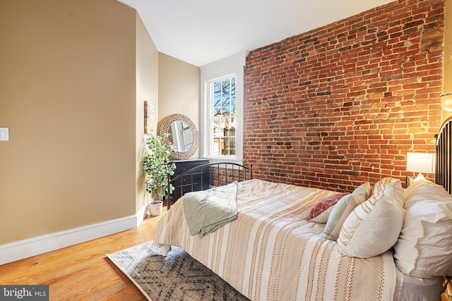 bedroom with hardwood / wood-style floors and brick wall