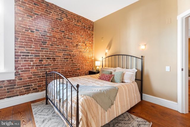 bedroom with hardwood / wood-style flooring and brick wall