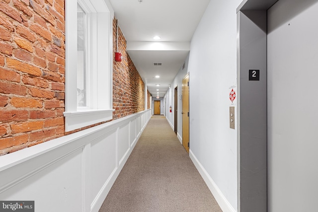 hall featuring elevator, brick wall, and carpet