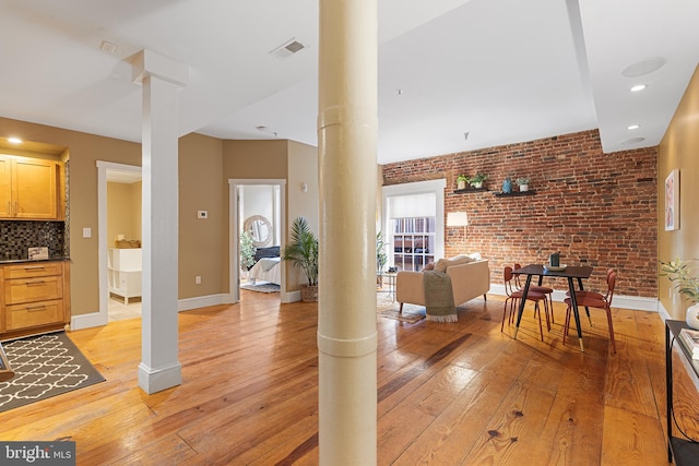 living room with ornate columns, brick wall, and light hardwood / wood-style flooring