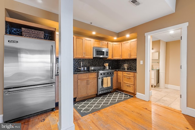 kitchen featuring light brown cabinets, high quality appliances, light wood-type flooring, and decorative backsplash