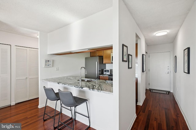 kitchen with stainless steel appliances, dark wood-type flooring, sink, and light stone countertops