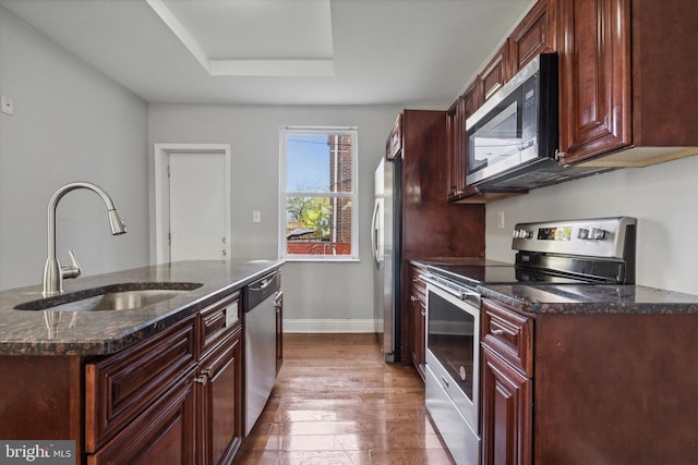 kitchen with hardwood / wood-style flooring, sink, a raised ceiling, appliances with stainless steel finishes, and dark stone countertops