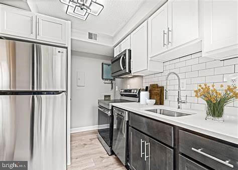 kitchen featuring sink, backsplash, light hardwood / wood-style floors, white cabinets, and appliances with stainless steel finishes