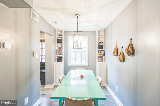 dining space featuring hardwood / wood-style floors, built in features, a textured ceiling, and an inviting chandelier