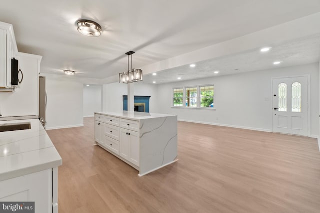 kitchen with light stone countertops, a kitchen island, light hardwood / wood-style floors, decorative light fixtures, and white cabinets