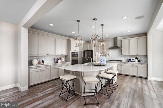 kitchen with hardwood / wood-style flooring, appliances with stainless steel finishes, a kitchen breakfast bar, an island with sink, and wall chimney range hood