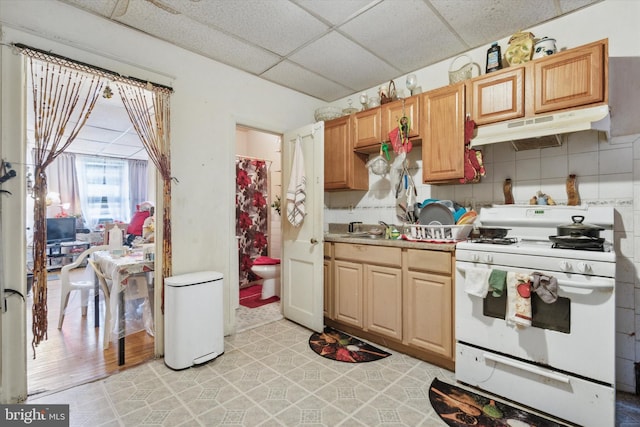 kitchen with white gas stove, a paneled ceiling, sink, backsplash, and light wood-type flooring