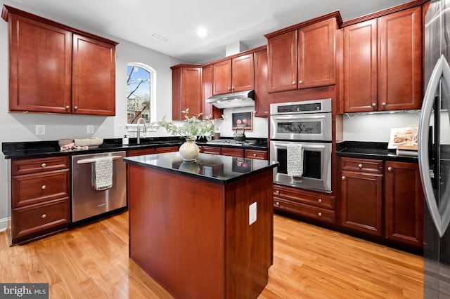 kitchen featuring stainless steel appliances, a kitchen island, sink, and light wood-type flooring