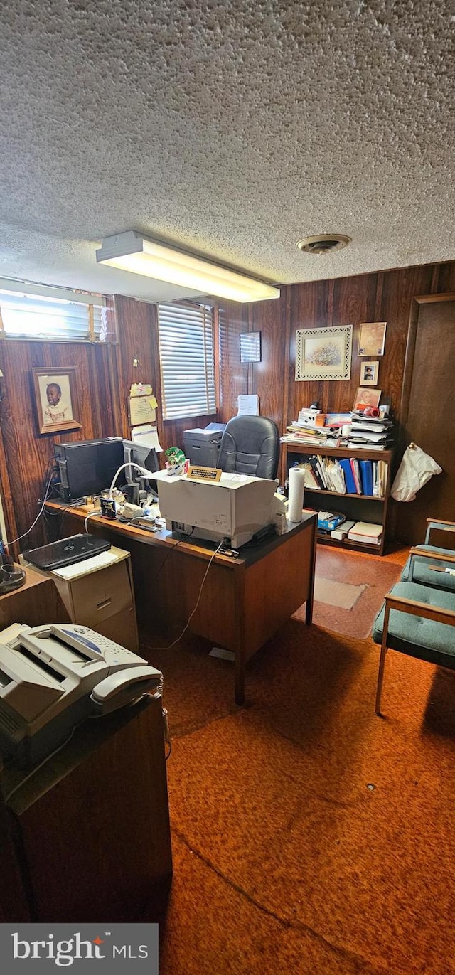 carpeted office space featuring wooden walls and a textured ceiling