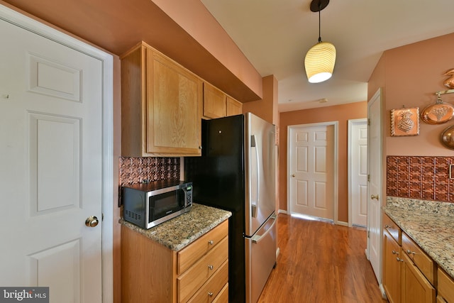 kitchen featuring light hardwood / wood-style flooring, tasteful backsplash, light stone countertops, appliances with stainless steel finishes, and decorative light fixtures