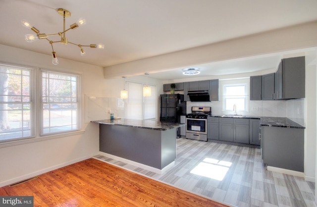 kitchen with stainless steel range with gas cooktop, kitchen peninsula, decorative light fixtures, light hardwood / wood-style flooring, and black refrigerator