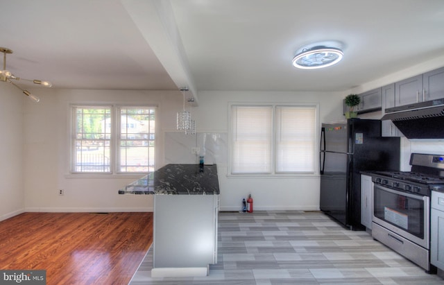 kitchen with dark stone counters, kitchen peninsula, stainless steel range with gas cooktop, gray cabinets, and light hardwood / wood-style flooring