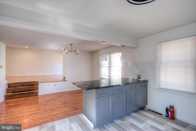 kitchen featuring kitchen peninsula, dark stone countertops, hanging light fixtures, a chandelier, and light hardwood / wood-style flooring