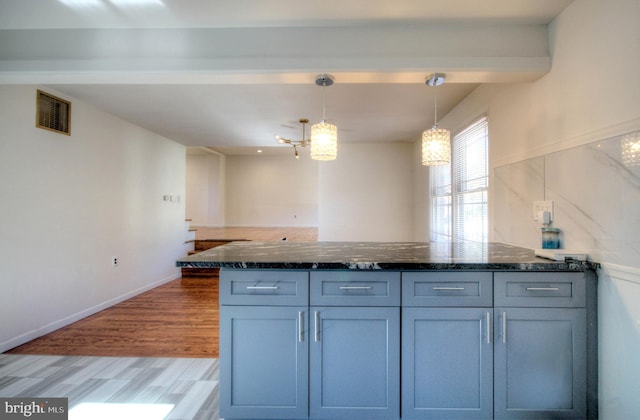 kitchen featuring dark stone counters, light hardwood / wood-style floors, and pendant lighting