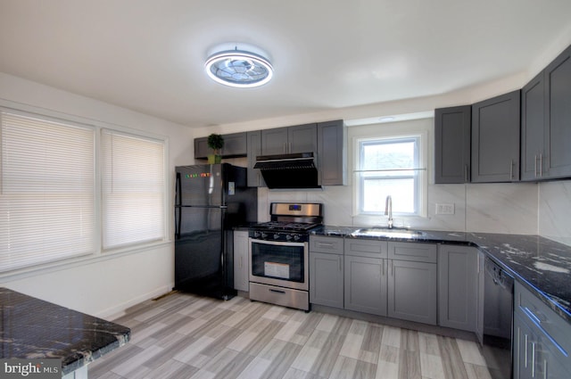 kitchen with black appliances, light wood-type flooring, sink, and dark stone countertops