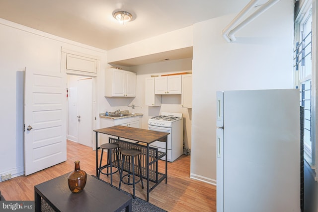 kitchen with white cabinetry, white appliances, sink, and light hardwood / wood-style floors