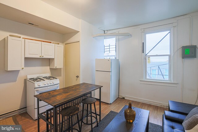 kitchen with a wealth of natural light, light hardwood / wood-style flooring, white appliances, and white cabinets