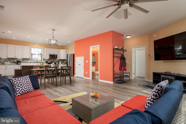 living room with ceiling fan with notable chandelier and light hardwood / wood-style floors