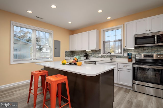 kitchen featuring white cabinetry, tasteful backsplash, light hardwood / wood-style floors, a kitchen island, and appliances with stainless steel finishes