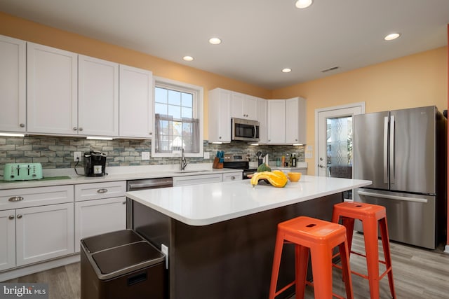 kitchen featuring a kitchen bar, a center island, stainless steel appliances, and white cabinetry