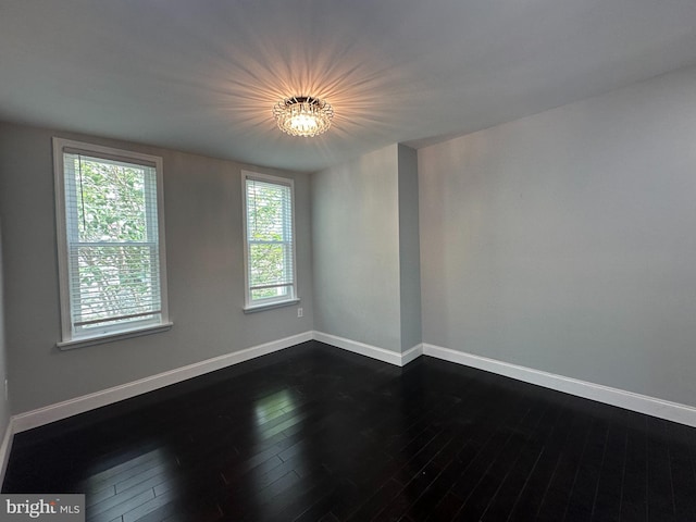 empty room with a wealth of natural light, dark hardwood / wood-style floors, and a chandelier