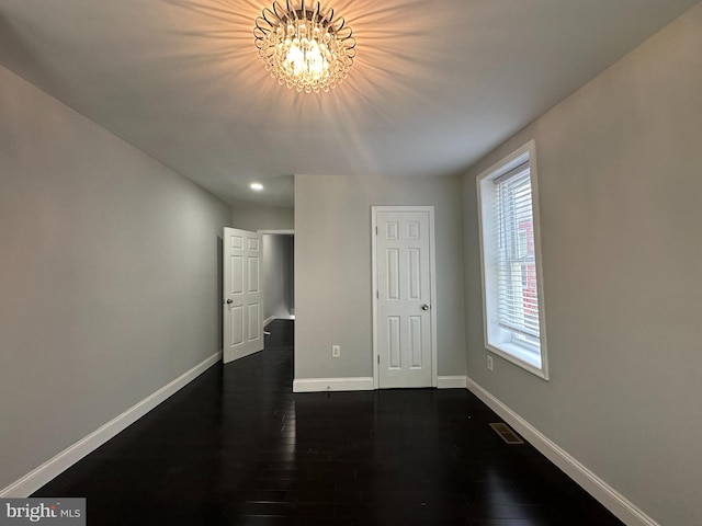 empty room with dark wood-type flooring and a notable chandelier