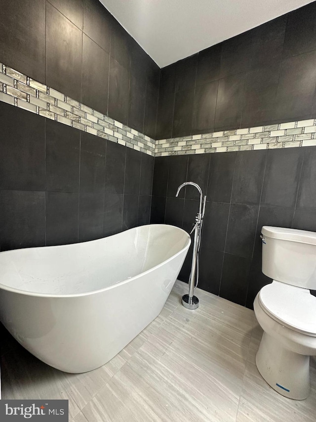 bathroom with tile patterned flooring, toilet, a bathtub, and tile walls