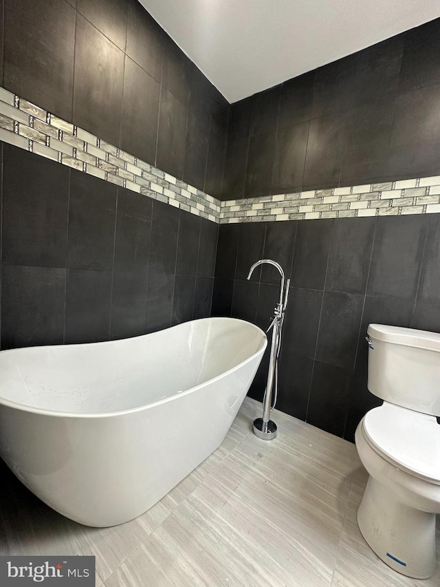 bathroom with a bathtub, tile walls, toilet, and tile patterned flooring