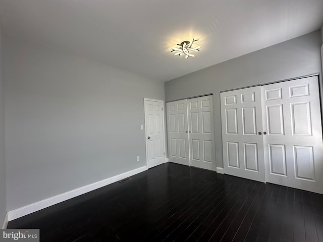 unfurnished bedroom featuring dark hardwood / wood-style flooring and two closets