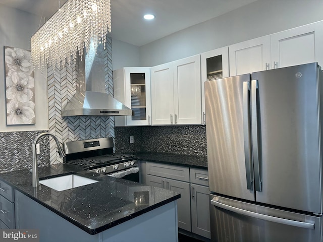 kitchen with tasteful backsplash, wall chimney range hood, appliances with stainless steel finishes, white cabinets, and dark stone countertops