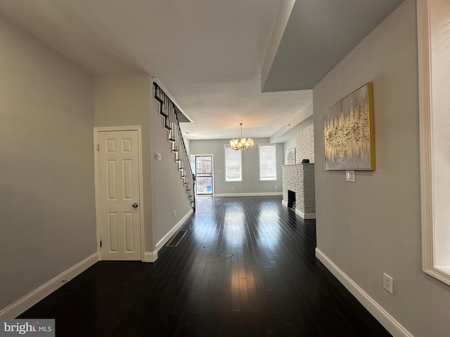 corridor with dark wood-type flooring, brick wall, and an inviting chandelier