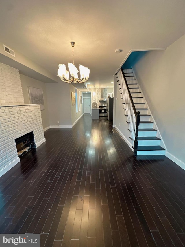 unfurnished living room featuring dark hardwood / wood-style flooring, an inviting chandelier, and a brick fireplace