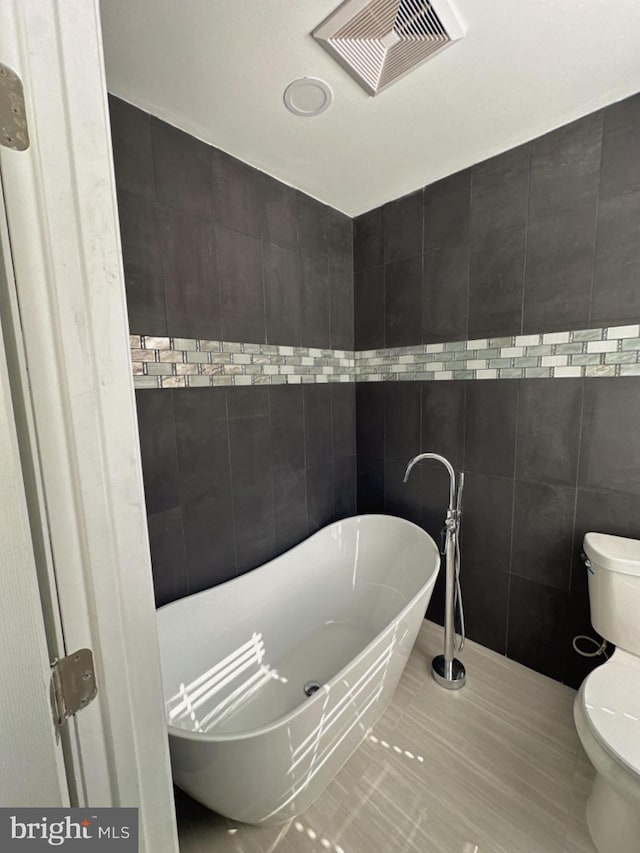 bathroom featuring tile patterned floors, a washtub, toilet, and tile walls