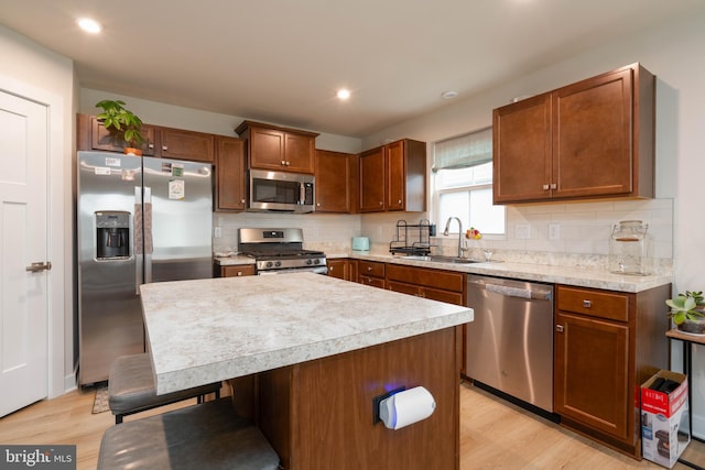 kitchen featuring sink, a center island, stainless steel appliances, a kitchen bar, and light wood-type flooring