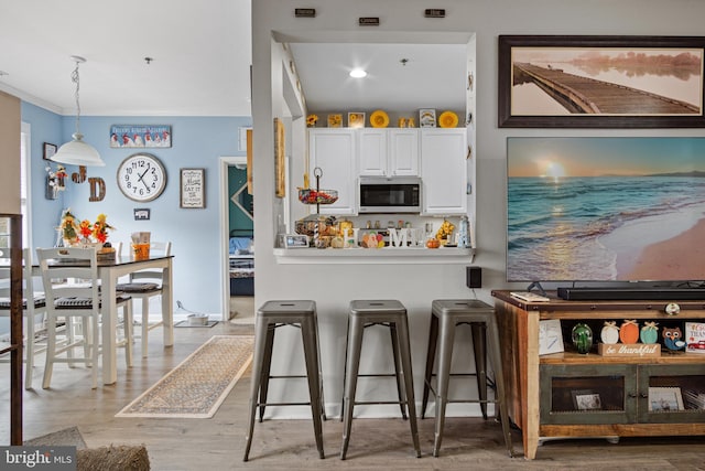 kitchen with pendant lighting, light wood-type flooring, white cabinetry, and a breakfast bar area