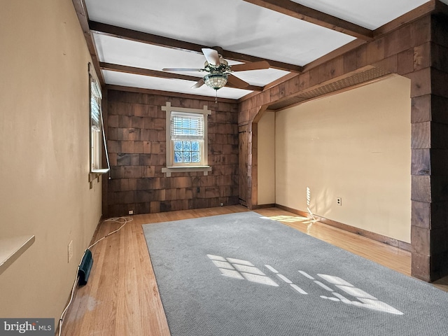 empty room with wood walls, ceiling fan, light hardwood / wood-style floors, and beam ceiling