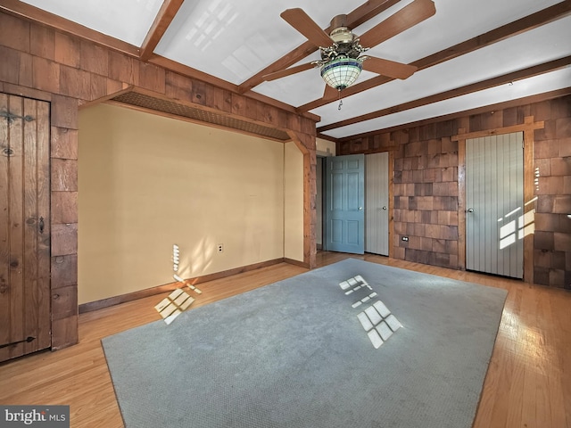 unfurnished living room featuring light wood-type flooring, beamed ceiling, wood walls, and ceiling fan