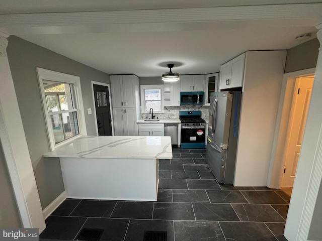 kitchen with kitchen peninsula, light stone countertops, stainless steel appliances, sink, and white cabinets