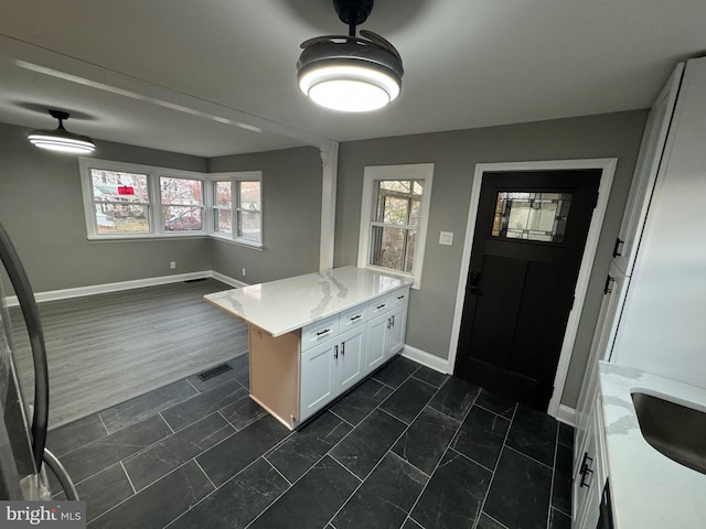 kitchen featuring a wealth of natural light, white cabinetry, kitchen peninsula, and light stone counters