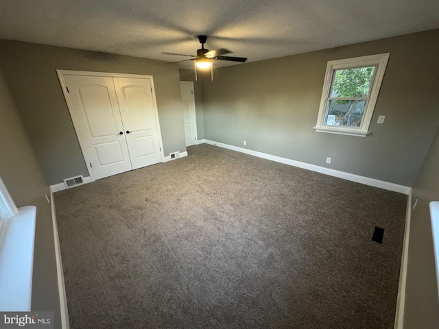 unfurnished bedroom featuring dark colored carpet, a textured ceiling, and ceiling fan