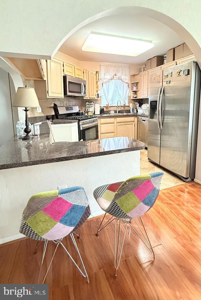 kitchen featuring light wood-type flooring, appliances with stainless steel finishes, sink, a kitchen breakfast bar, and kitchen peninsula