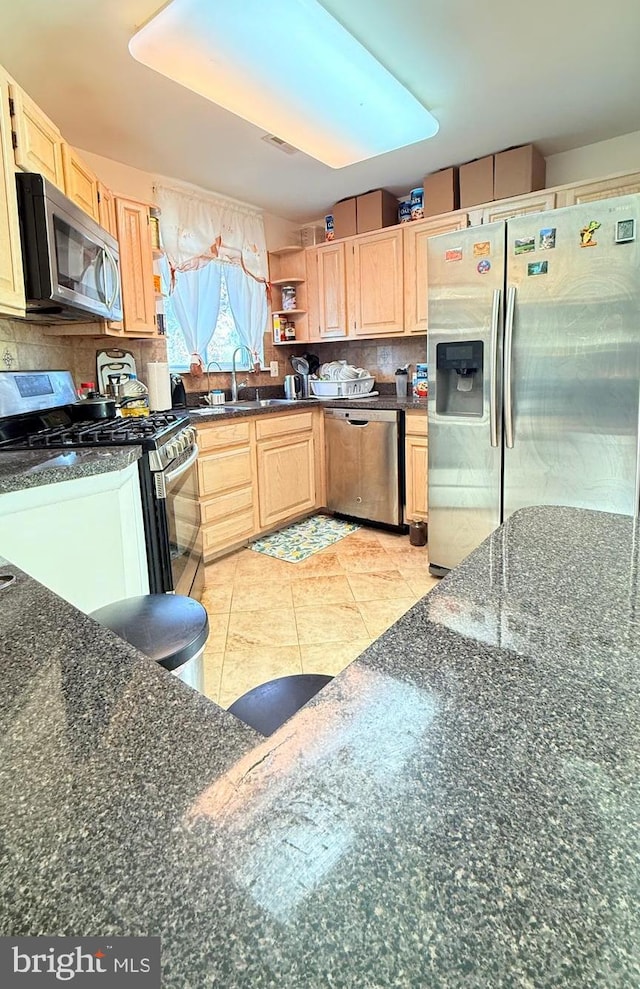 kitchen featuring dark stone counters, light brown cabinetry, appliances with stainless steel finishes, and sink