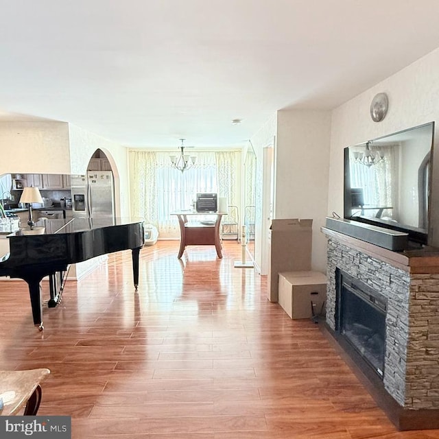 misc room with wood-type flooring, a healthy amount of sunlight, a stone fireplace, and a chandelier