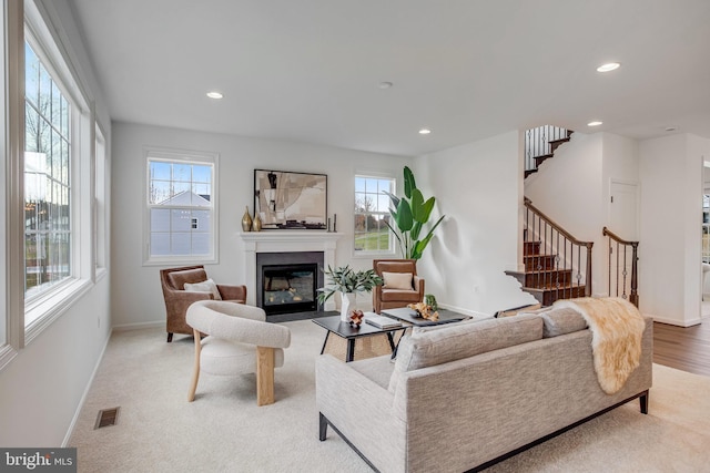 carpeted living room with stairway, plenty of natural light, a glass covered fireplace, recessed lighting, and baseboards