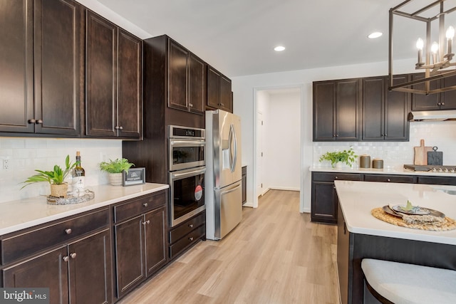 kitchen with stainless steel appliances, hanging light fixtures, backsplash, dark brown cabinets, and light wood-type flooring